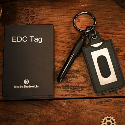 EDC Tag keychain on a wooden surface with a book and small box.